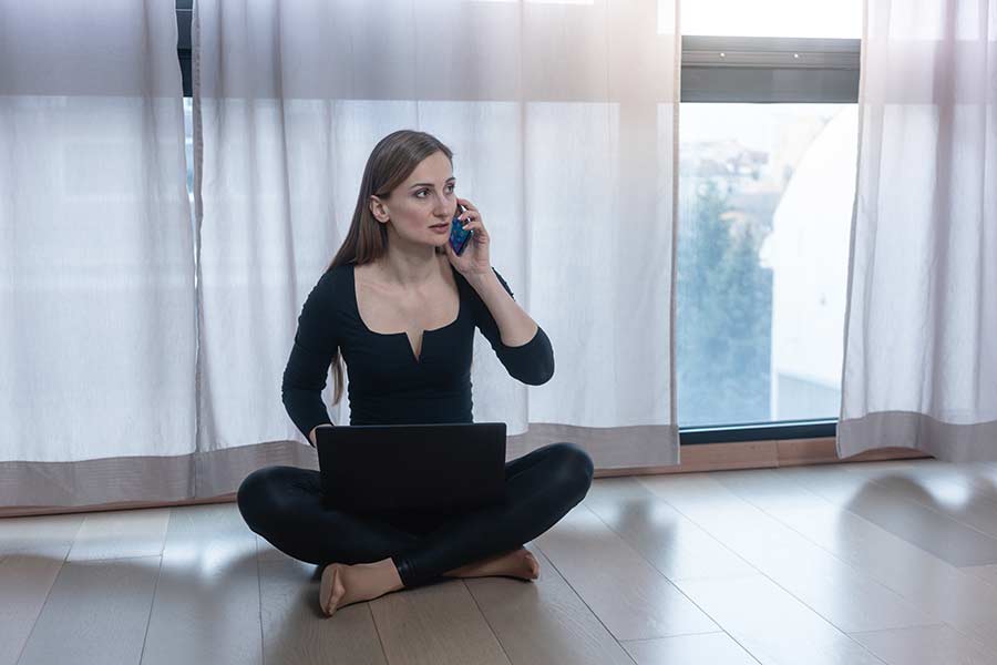 Mujer joven hablando por celular, sentada en el piso de su casa