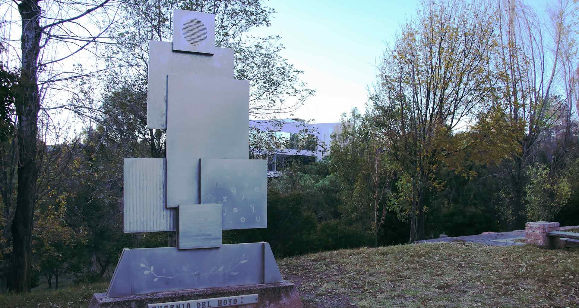 Imagen del monumento en Memoria a Don Eugenio del Hoyo, a un costado de cafeteria, se muestran varias figuras rectangulares, acomodadas una sobre la otra y articuladas verticalmente.