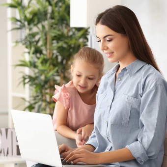 Madre de familia trabajando en su laptop, con su hija a una lado